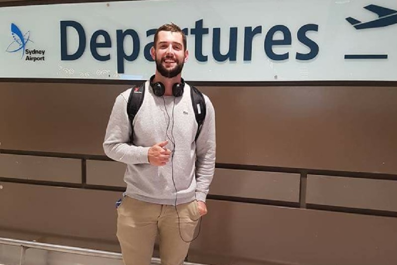 Baxter Reid standing in front of a Sydney Airport departure sign.