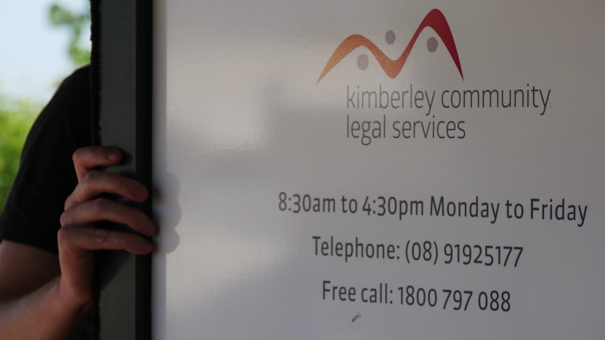 A hand pushing a white door open which has a sign that says Kimberley Community Legal Services.
