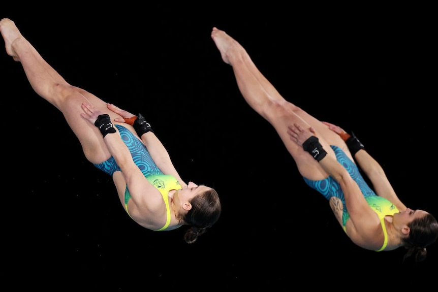 divers captured in motion in the air with their legs outstretched wearing green and gold australian swimmers