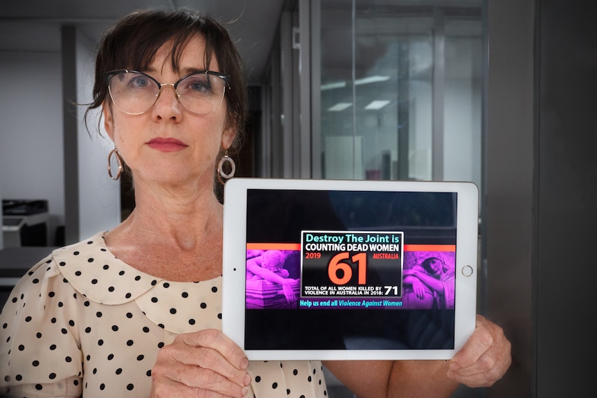 A woman holding an iPad with a graphic on it saying destroy the Joint, counting dead woman, total women killed in 2019 is 61.