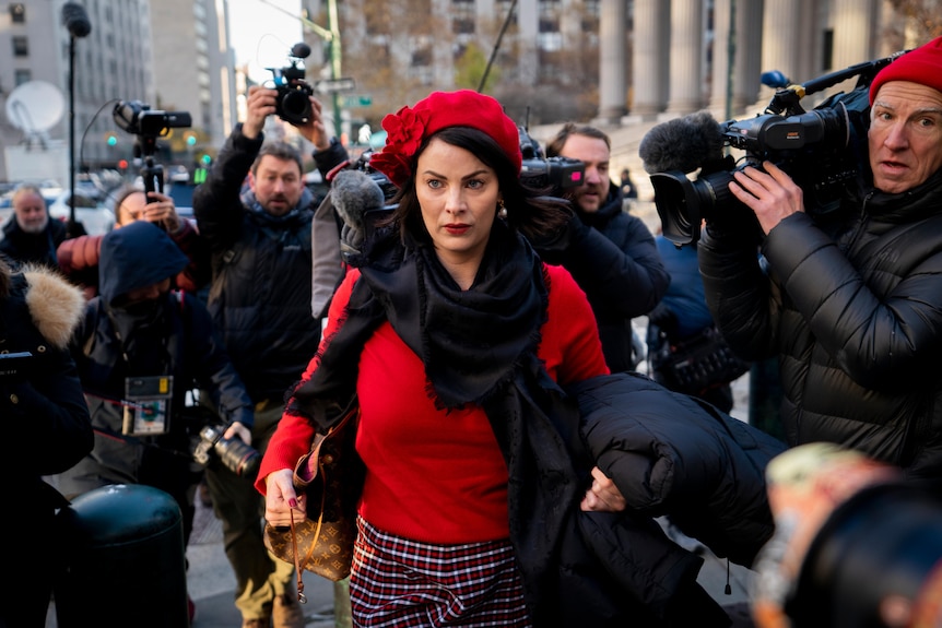 A woman walks through a crowd of photographers on a city street.