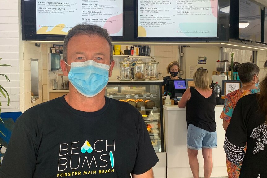 A man in a black T-shirt and mask in a cafe.