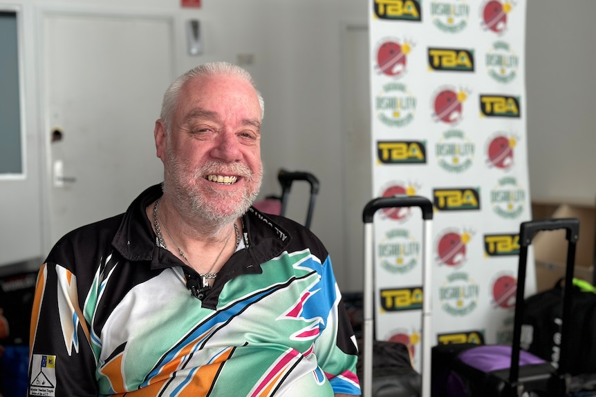 A man wearing a multi-colored bowling shirt smiles.