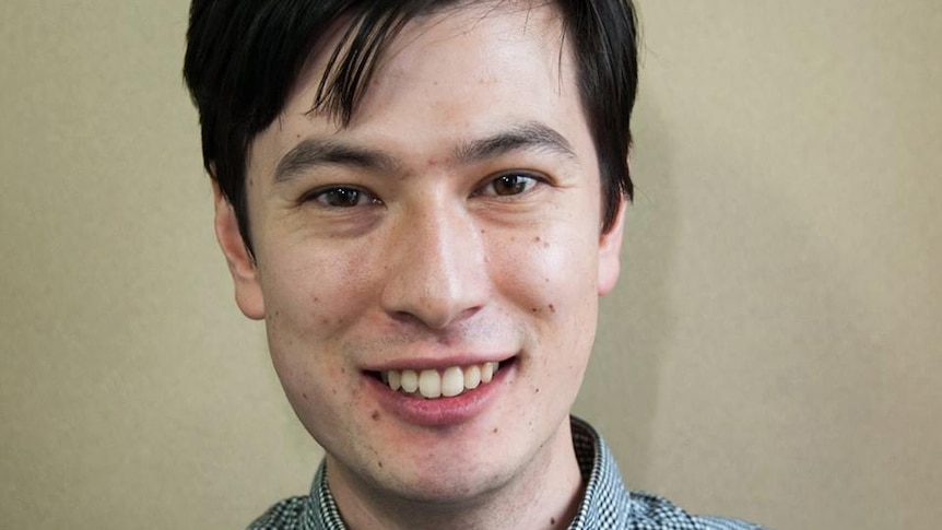 A headshot of a smiling man wearing a checked shirt.
