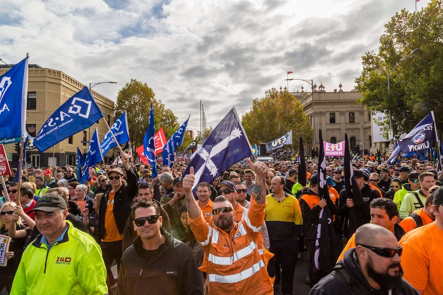 Thousands of union members with flags rally in Melbourne, calling for an increase to the minimum wage.