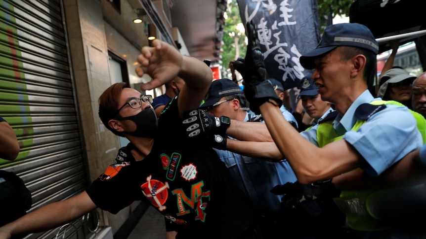 Several police officers reach out towards a man in a black face mask and clothing.