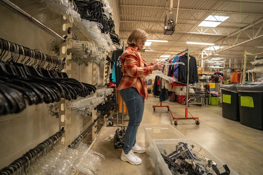 A woman arranges coat hangers inside a clothing store 