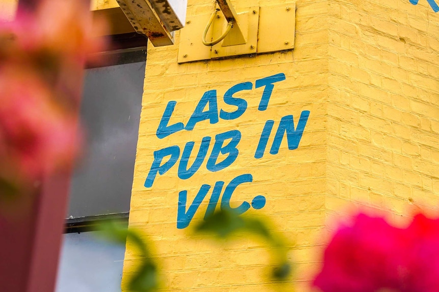 A yellow brick wall with the words 'last pub in Vic' painted in blue on it.