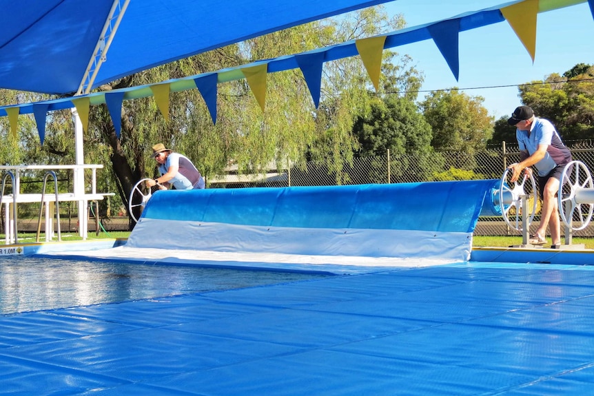 Two people unrolling a pool cover.