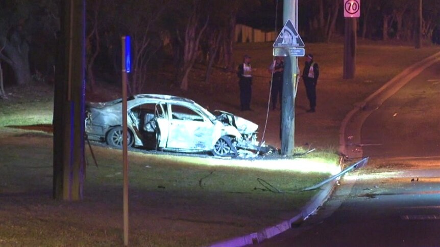 A damaged car next to an electricity pole.