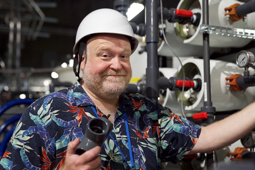 A man in a hardhat and brightly coloured shirt smiles at the camera.