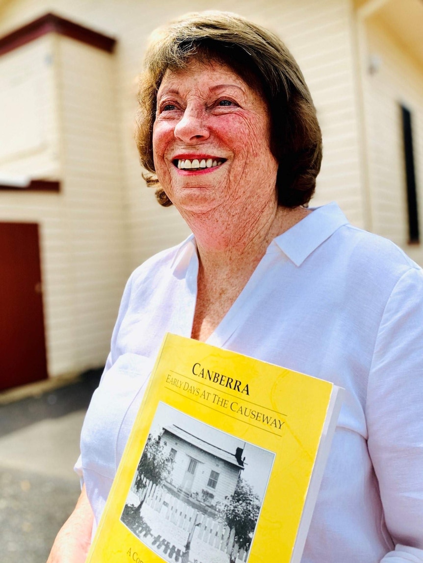 A smiling woman holds a book.