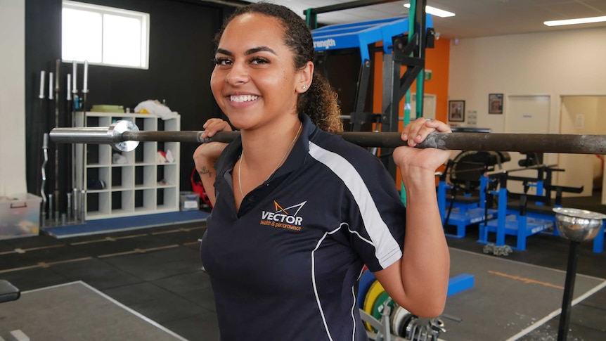 Rachel Warcon smiles at the camera with a bar on her shoulders.