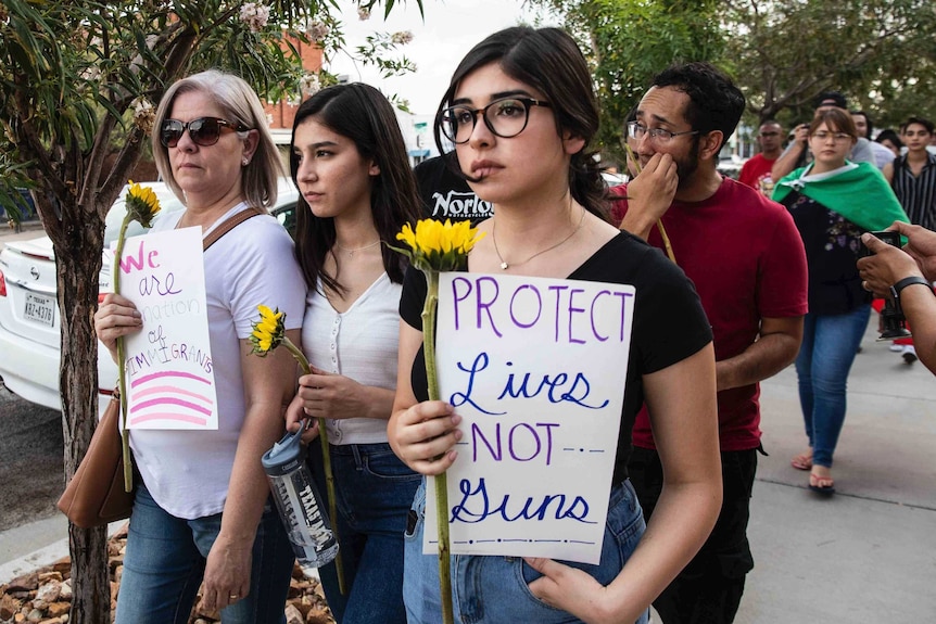 Three women look distantly, walking along the street while carrying signs.