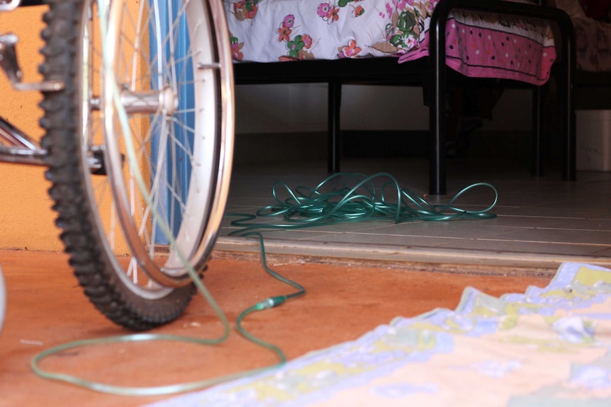 The door of a room with oxygen tank tubes on the ground and the wheel of a wheelchair in the front.