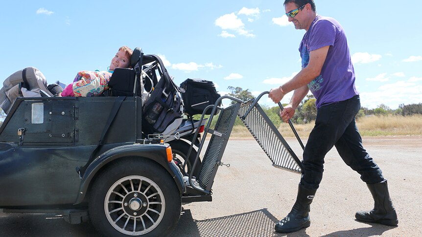 David Barker folds up a wheelchair ramp connected to his motorbike as his daughter Shanniah sits in the bike's sidecar.