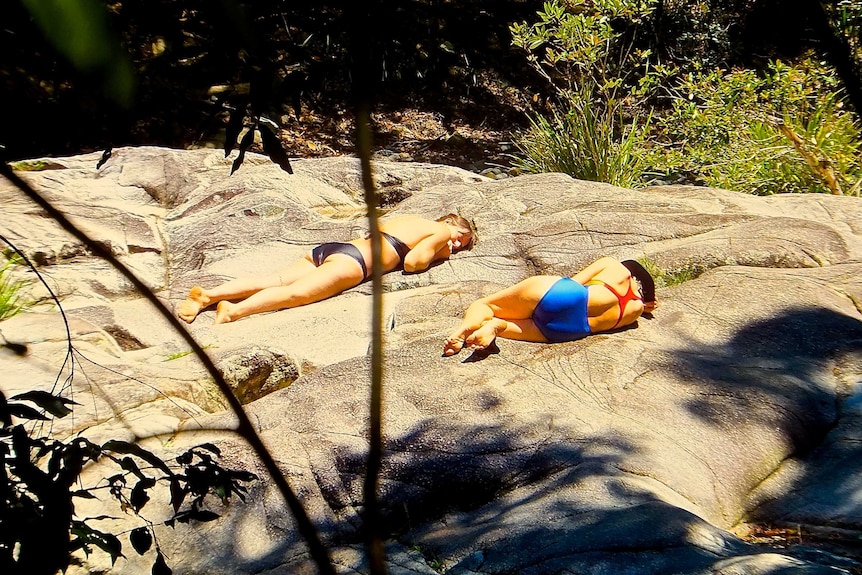 Two women lying on rocks at a Promised Land swimming hole near Bellingen.
