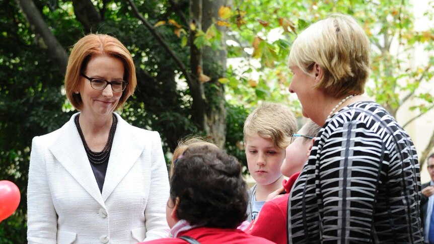 Julia Gillard and Jenny Macklin speak with a woman in a wheelchair at a morning tea in Melbourne.