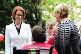 Julia Gillard and Jenny Macklin speak with a woman in a wheelchair at a morning tea in Melbourne.