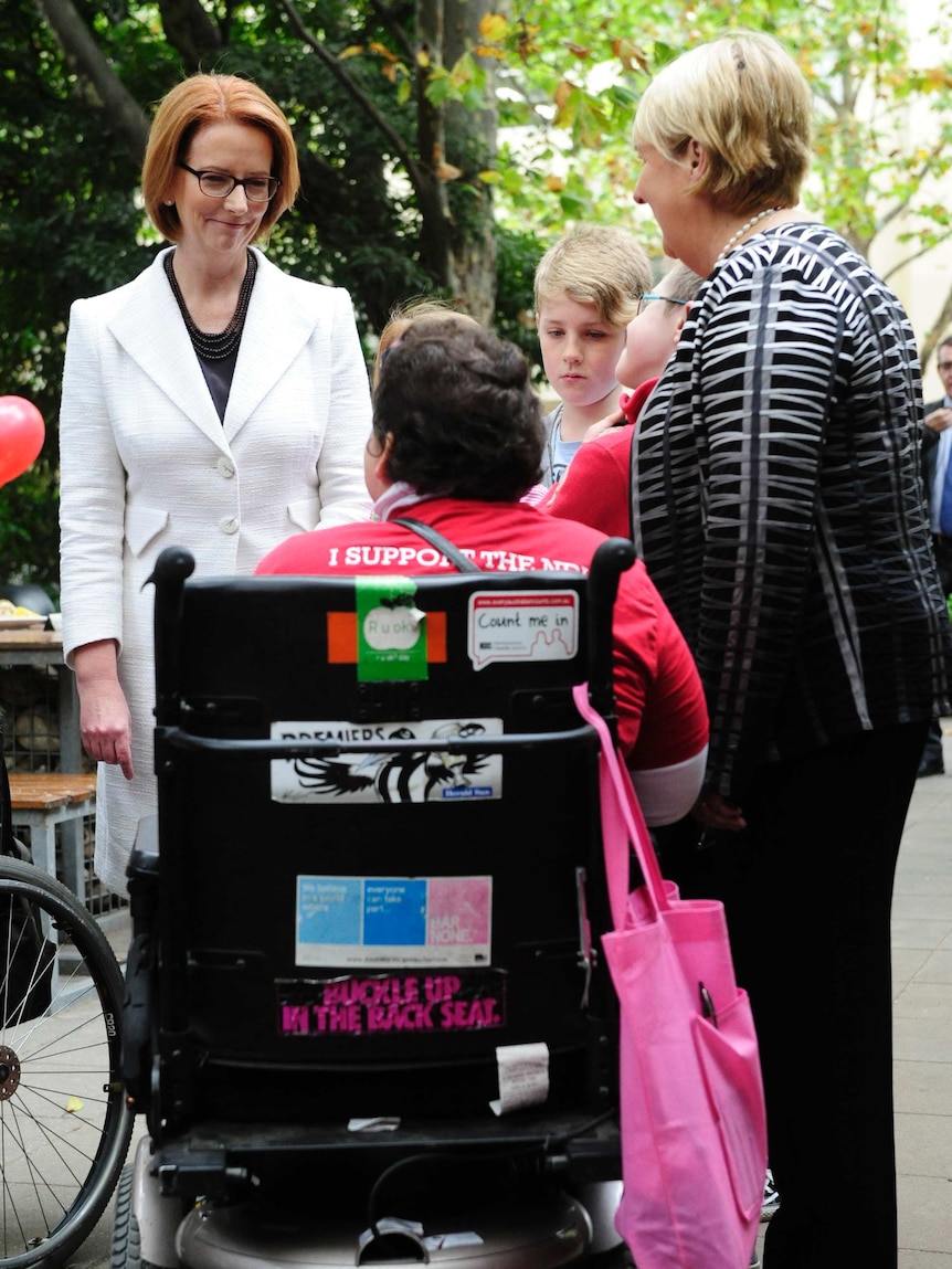 Julia Gillard and Jenny Macklin speak with a woman in a wheelchair at a morning tea in Melbourne.