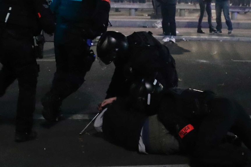 Police officer holds person on the ground as protesters look on