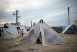 A girl sits in the doorway of a makeshift tent at a camp