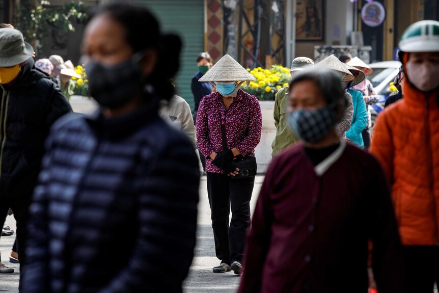 People wearing masks walk down a fairly crowded street in Vietnam.