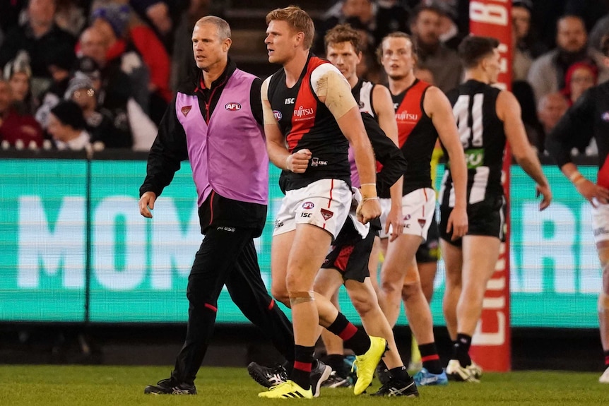 Michael Hurley walks off the ground favouring his right shoulder, being supported by a trainer in a pink vest