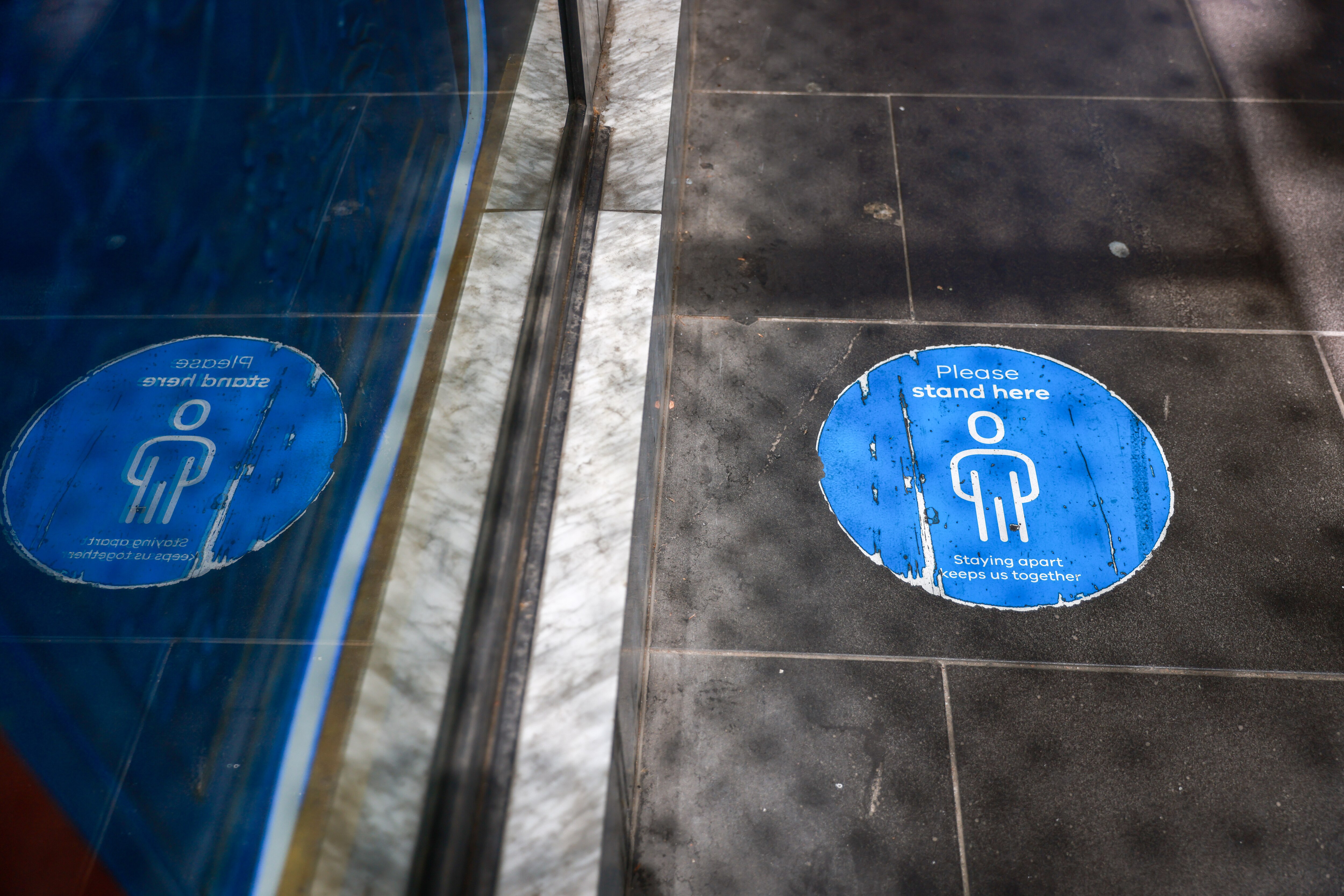 Faded social distance stickers on the footpath and people walking with masks as they pass hand sanitiser stations.