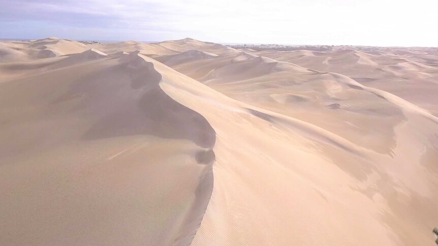 Wide shot from drone above showing white sandhill ridges and the blue ocean beyond