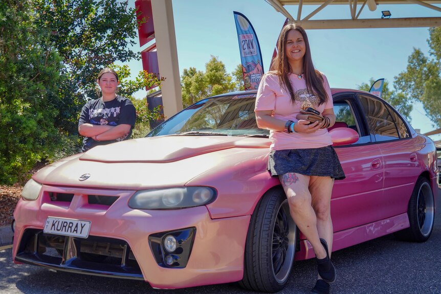 Two young women stand next to a pink sedan