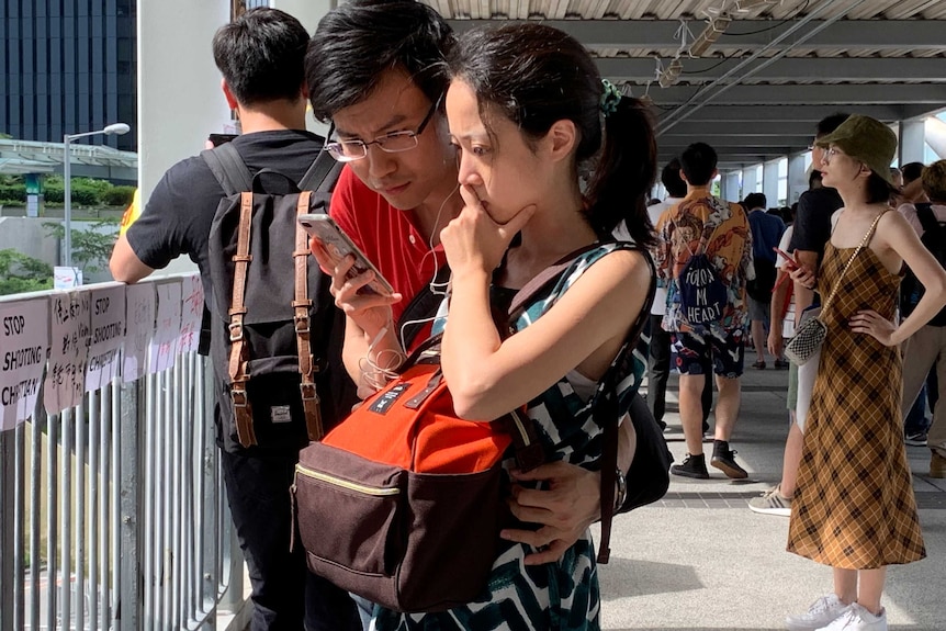 A couple share earbuds as they watch a video on a smartphone.