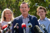 A close-up of Mark McGowan with his wife and one of his sons standing either side of him in front of microphones.