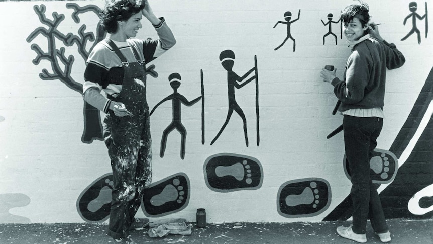 Black and white photo of two women painting a mural.