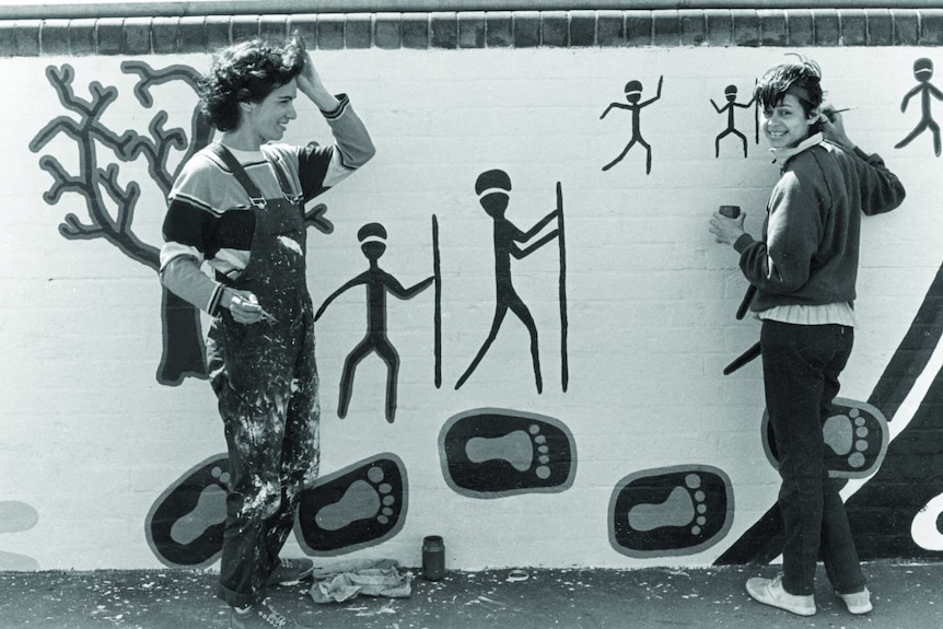 Black and white photo of two women painting a mural.