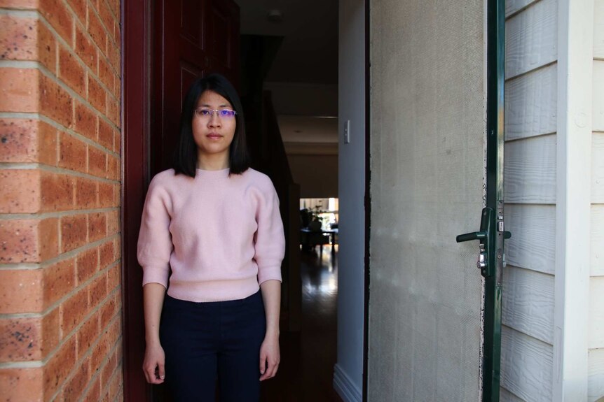 Mien Jeu Chang looks into the camera with a serious expression on her face as she stands in her doorway.