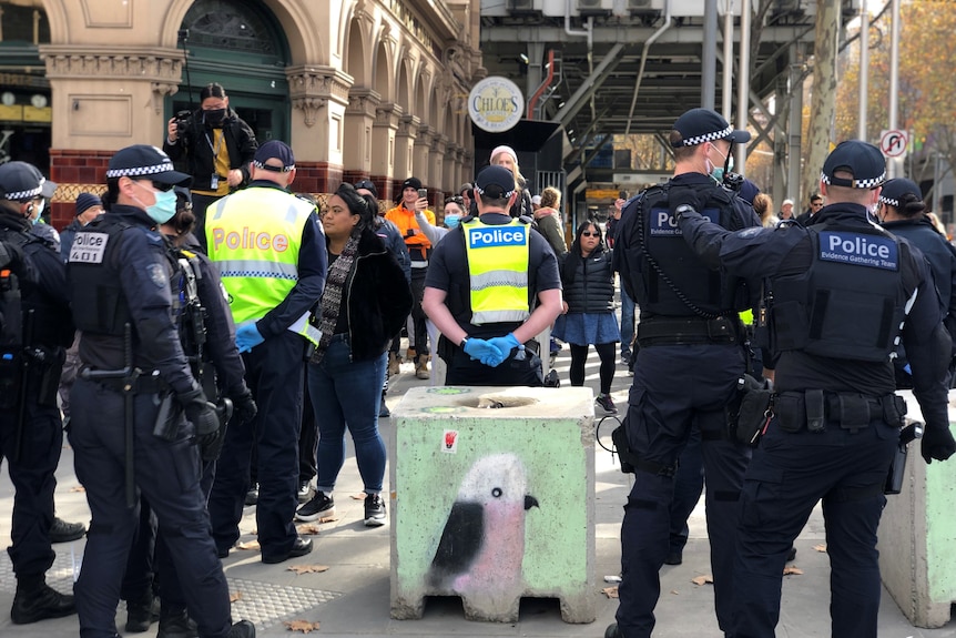 A large amount of police on a Melbourne street corner near some protesters.