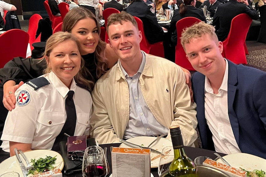 A woman in paramedic uniform sitting at a table with her three adult children at the awards night.