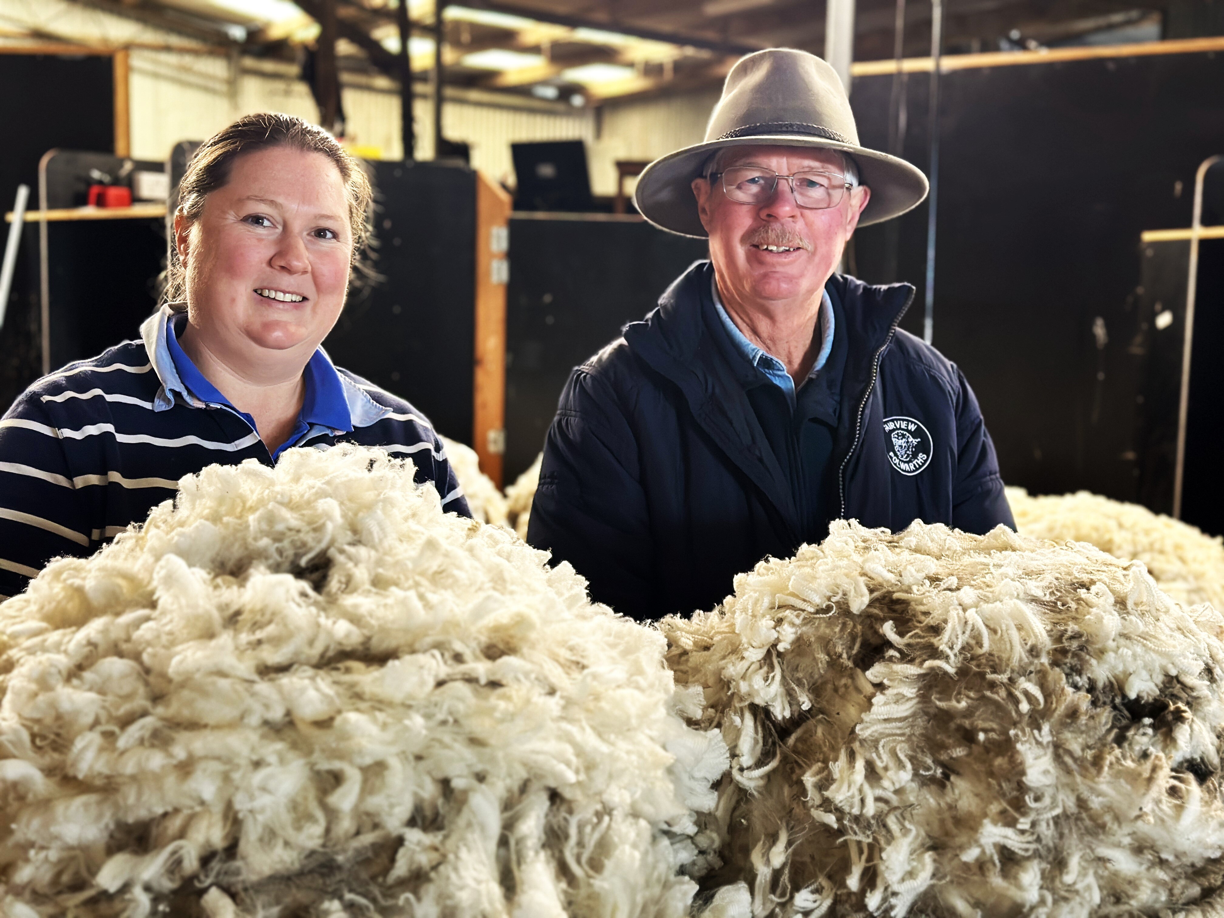 A woman and her father stand side by side with sheep's fleece in the foreground.