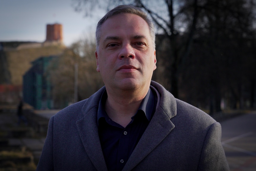 A man in a grey suit looks defiantly at the camera