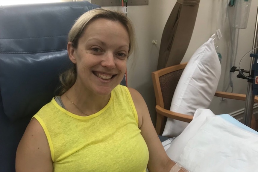 A woman in a yellow top sits on a chair with pillows.