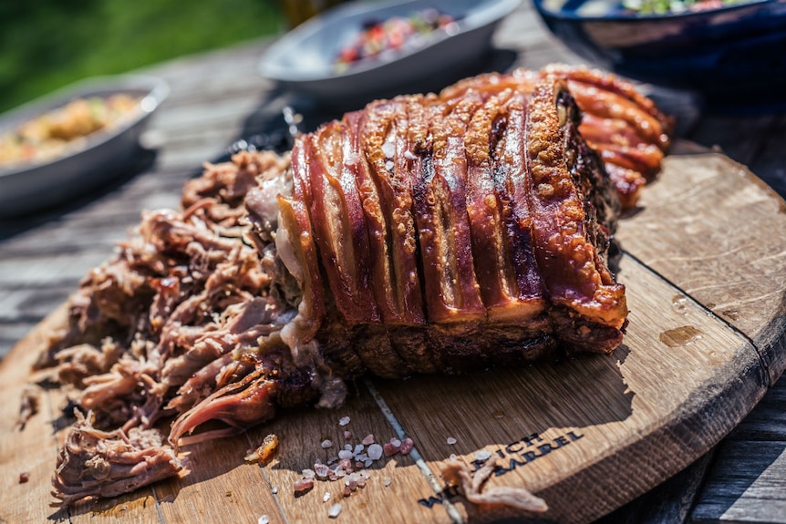 Roast pork on a wooden tray on an outside table with other food.