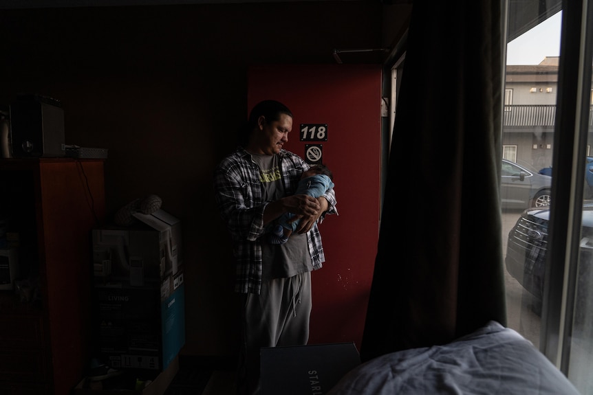 A man holds his baby in the doorway of a motel.