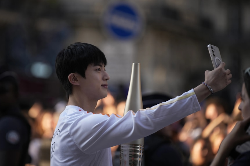 A South Korean man dressed in white takes a selfie with his phone