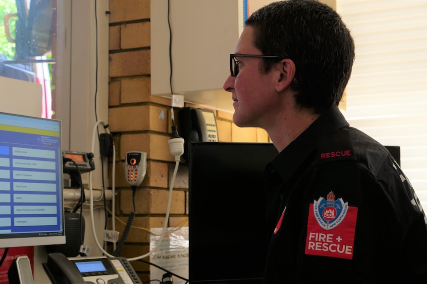 A female firefighter sits in the fire station office working on the computer 
