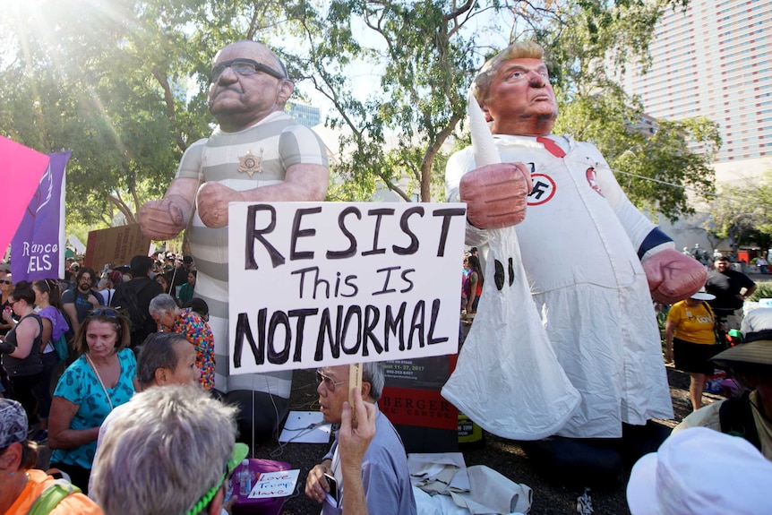 Activists hold two blow-up dolls of former Arizona sheriff Joe Arpaio in a prisoner's uniform and Donald Trump in a KKK outfit.
