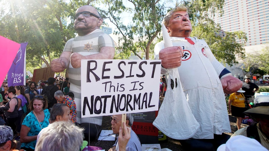 Activists hold two blow-up dolls of former Arizona sheriff Joe Arpaio in a prisoner's uniform and Donald Trump in a KKK outfit.