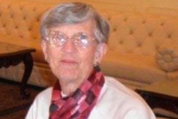 An elderly woman with short grey hair and glasses smiling at the camera.