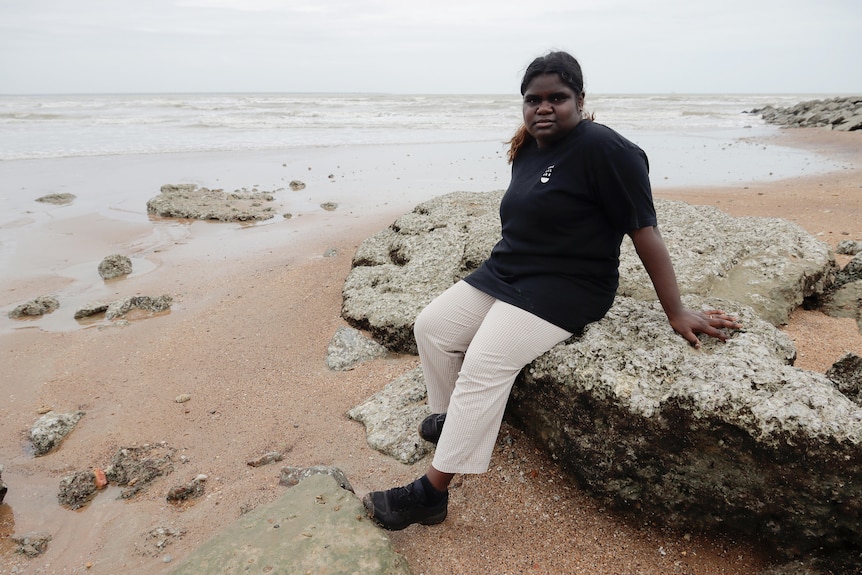an aboriginal woman sitting on a rock at the beach