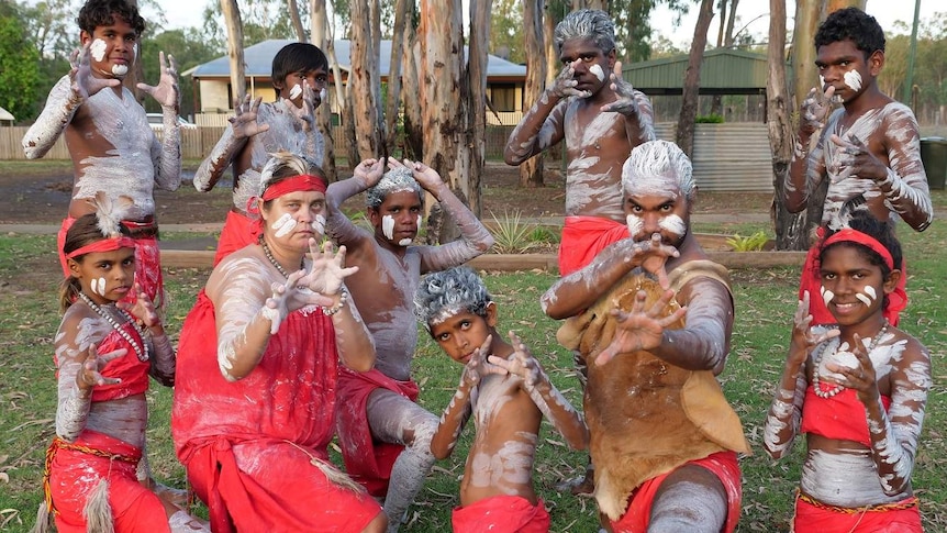 A group of indigenous girls and boys pose in their traditional paint and outfit in front of the camera.